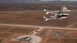 a white airplane flies over a long runway in a desert in this aerial view